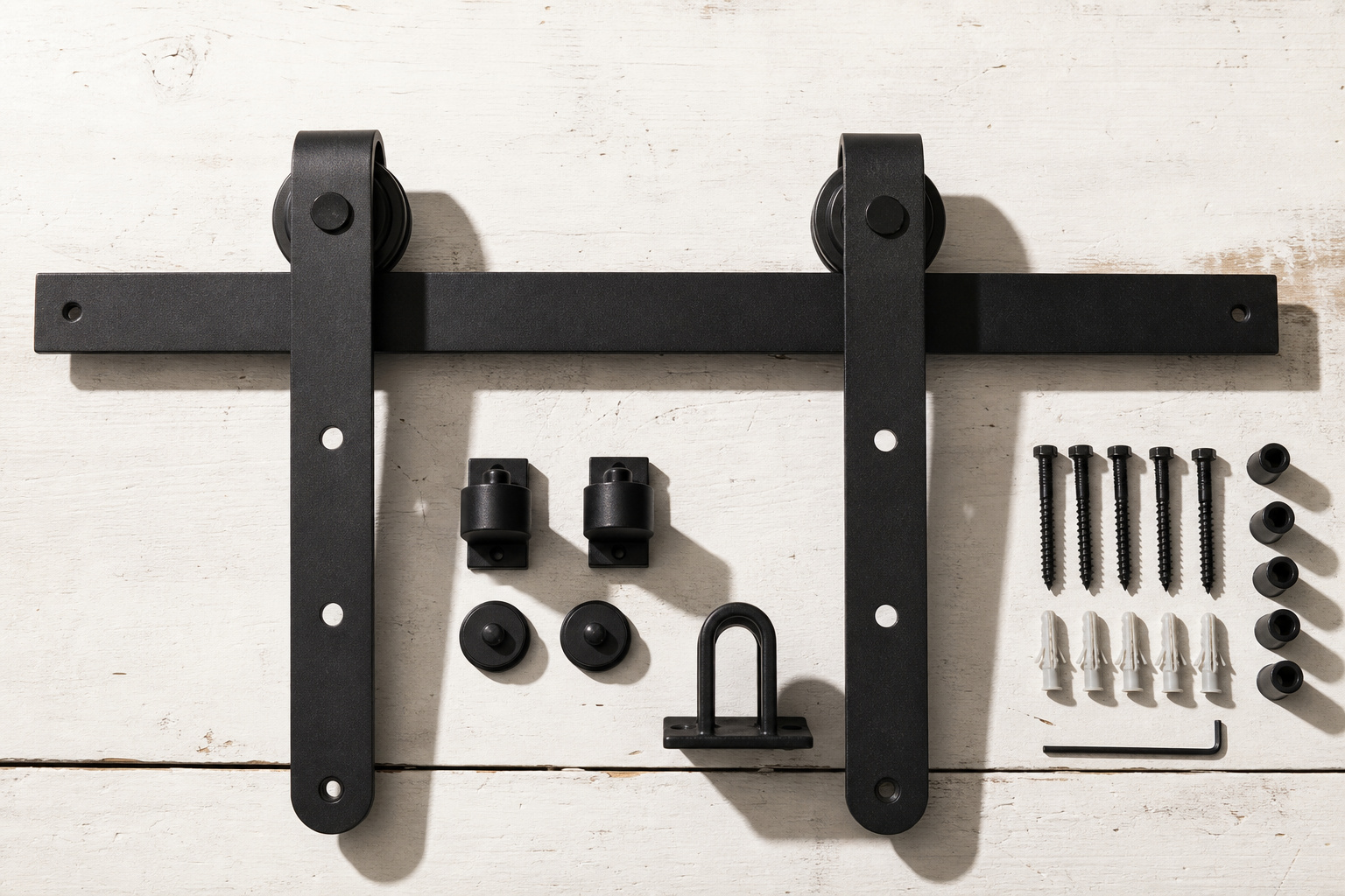 Complete barn door hardware kit components including flat track, J-strap hangers, door stoppers, floor guide and anti-jump discs laid out on a workbench