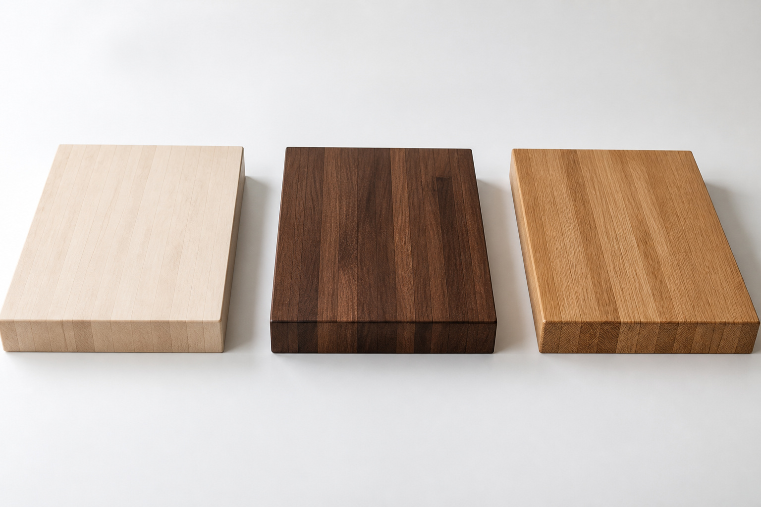 Three butcher block wood species side by side: pale hard maple, dark walnut, and warm white oak edge-grain slabs showing contrasting grain and colour
