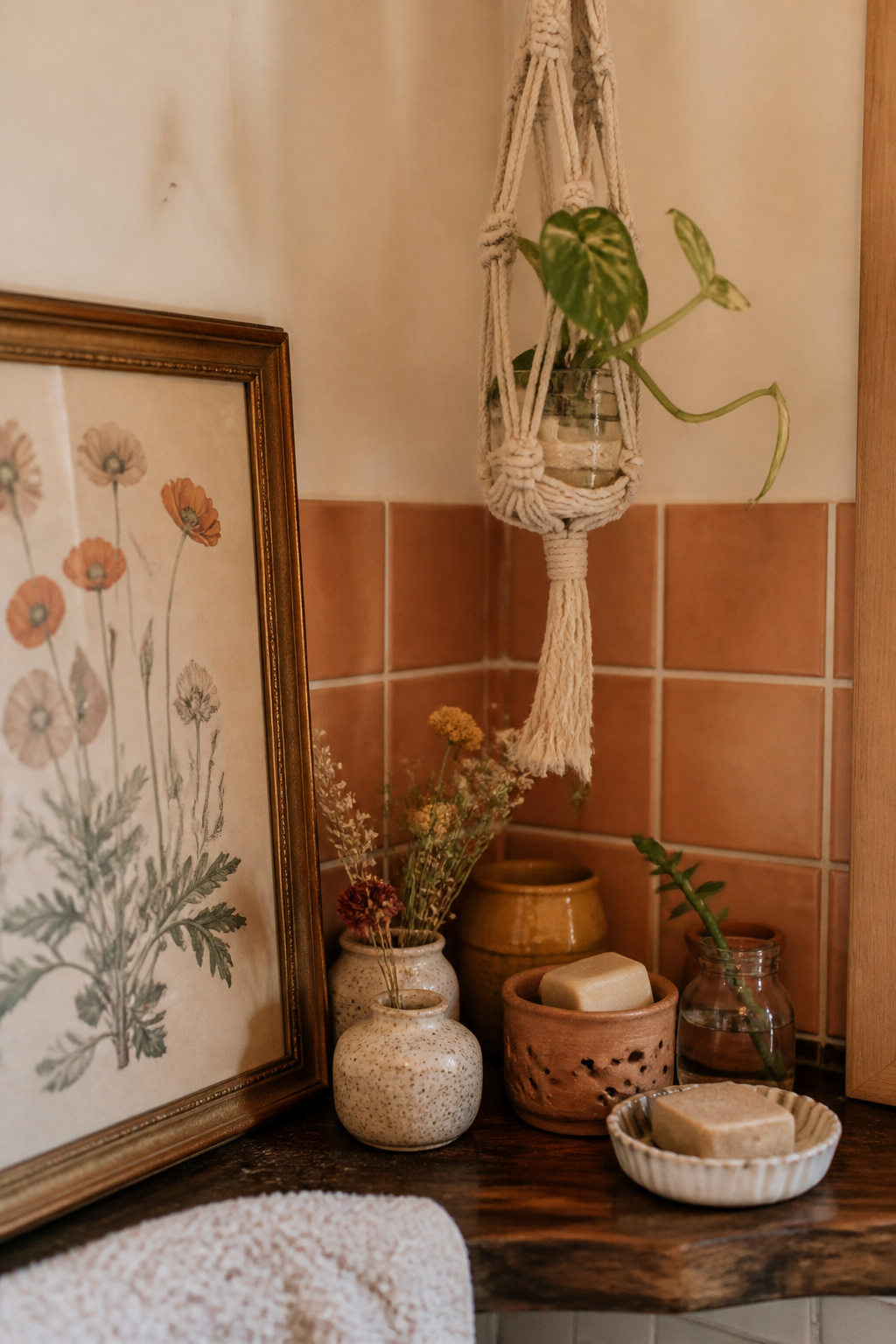 Budget boho bathroom shelf with thrifted ceramics, a handmade macramé hanger, peel-and-stick terracotta tile and a framed botanical print