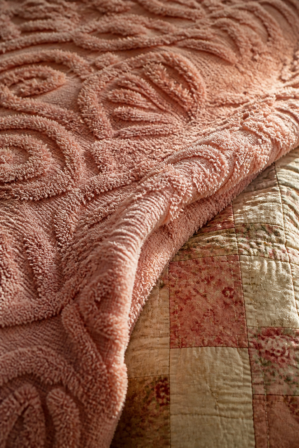 Vintage chenille bedspread draped as mid-layer over a patchwork quilt, raking light revealing the raised tufted pile
