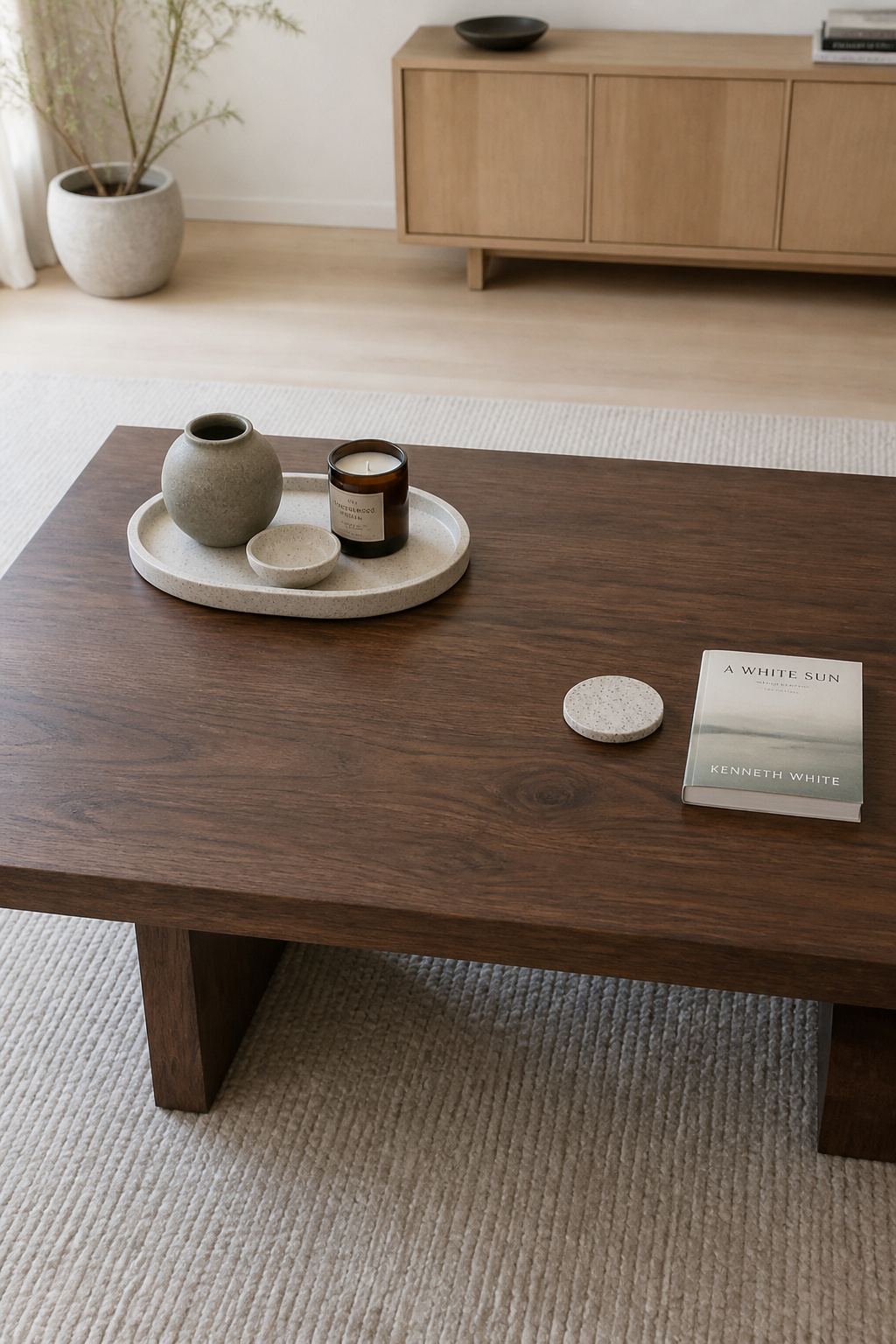 A stone tray placed off-centre on a walnut coffee table, leaving clear negative space around it where a coaster and paperback book rest on the bare tabletop