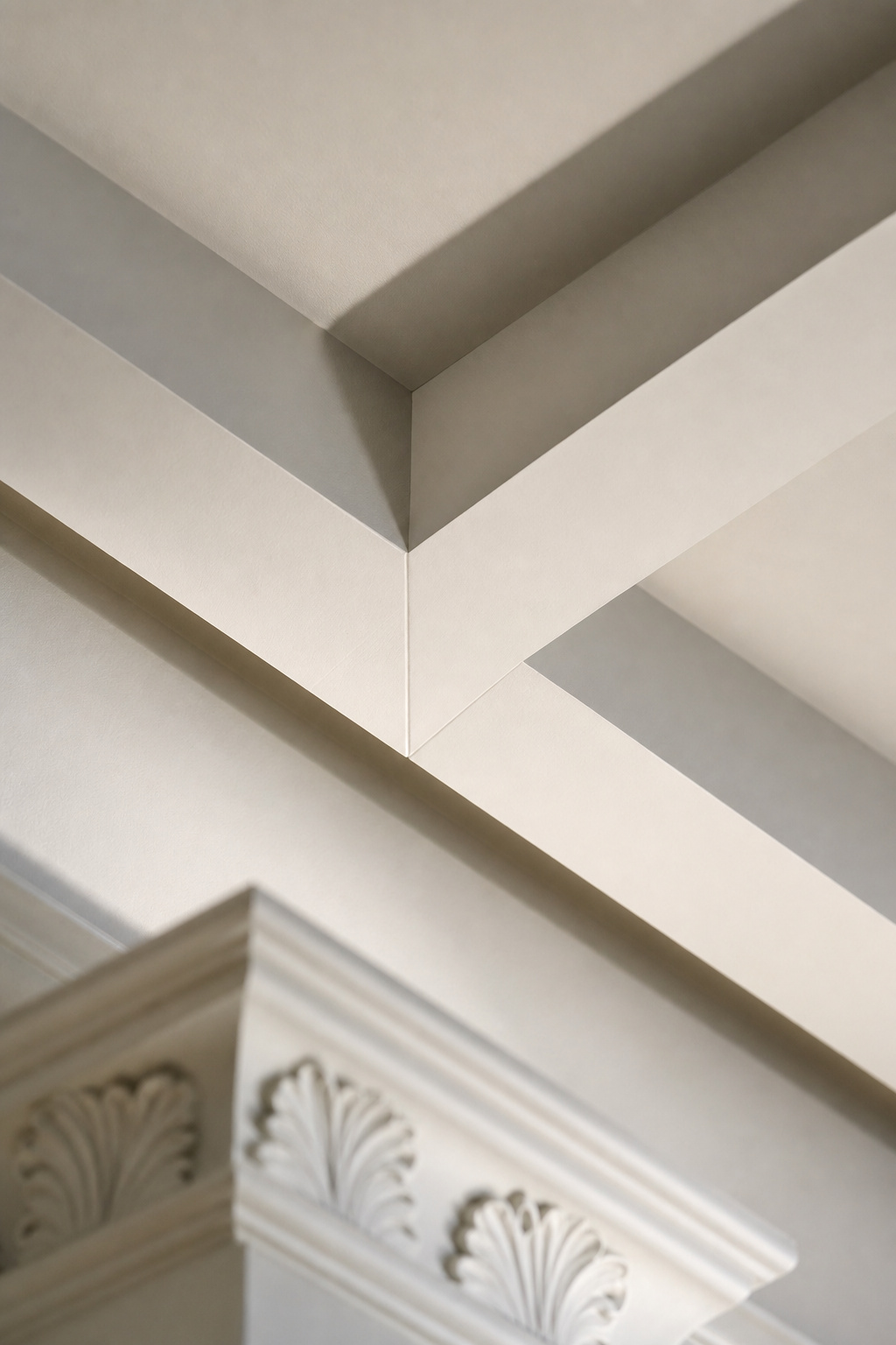 Close-up corner detail of coffered ceiling beams meeting at a right angle, deep shadow lines in the recessed panels against a white painted surface