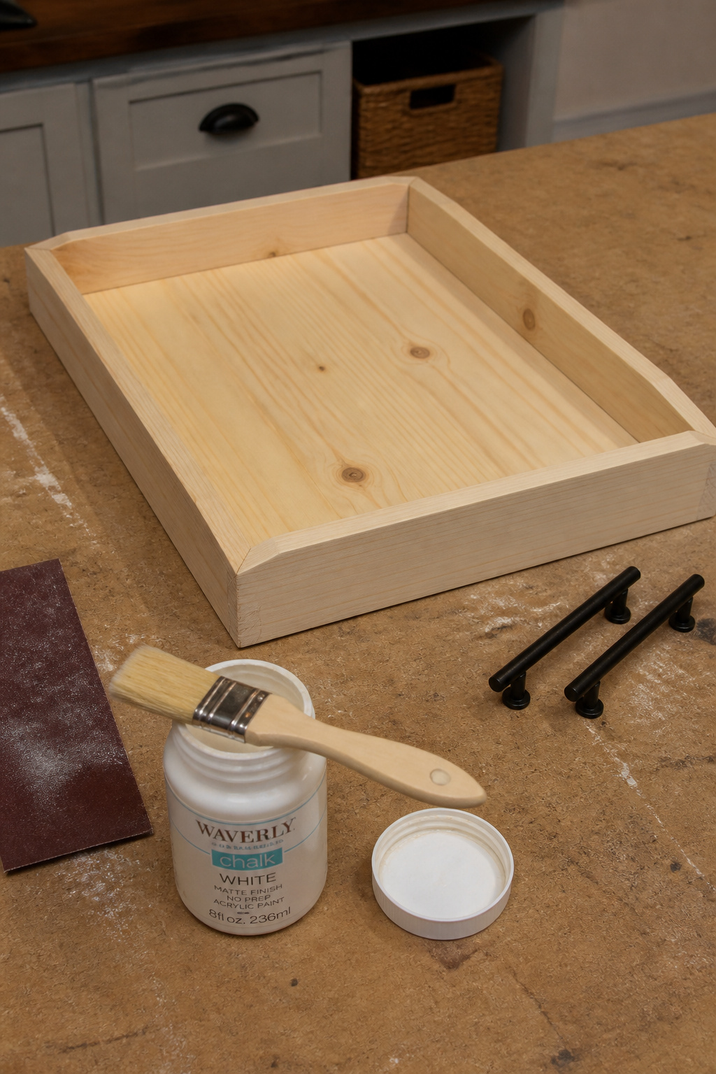 DIY pine coffee table tray in progress on a workbench, with assembled pine boards, chalk paint, and two black bar handles ready to attach