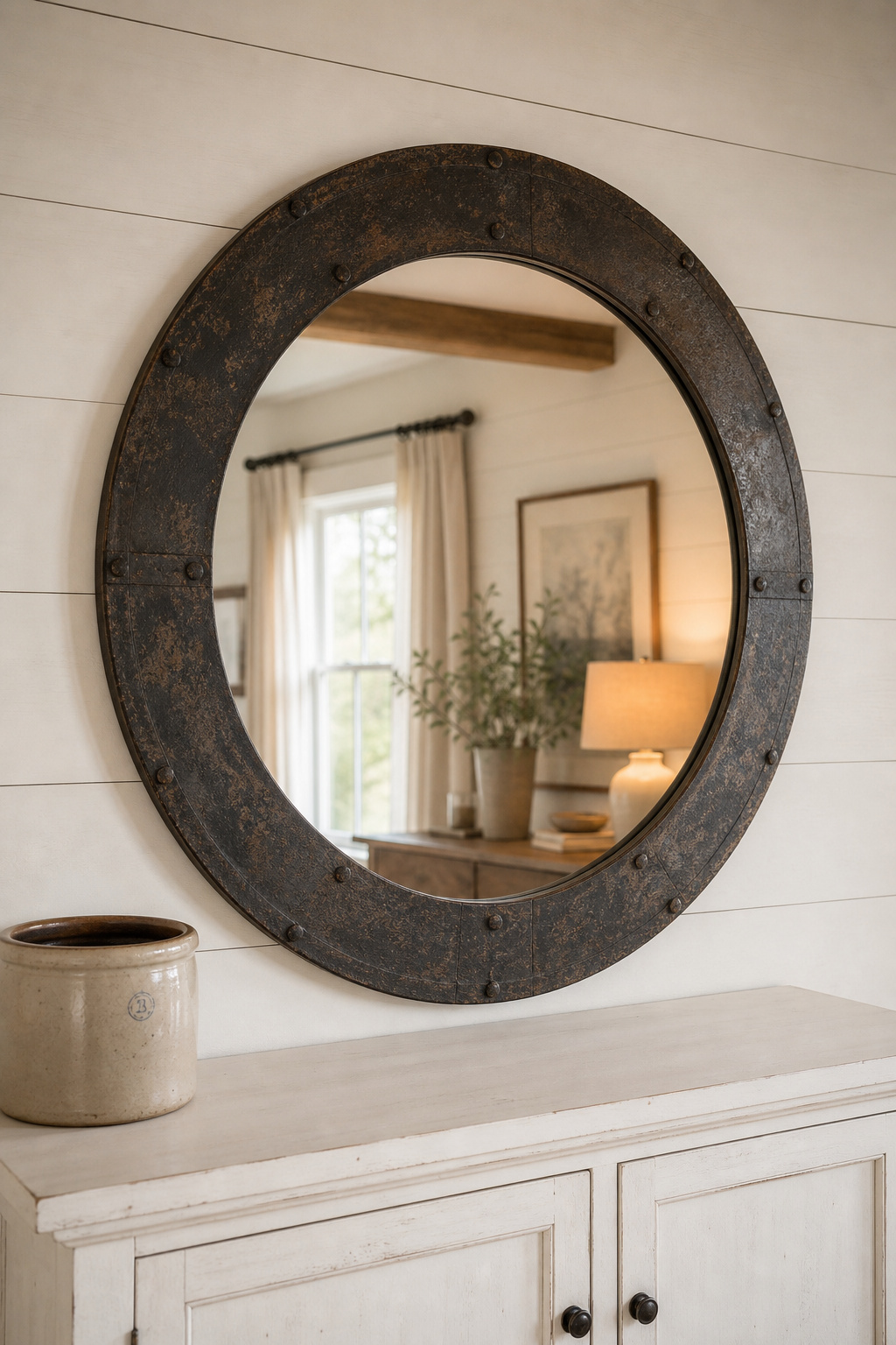 Round aged-iron mirror mounted above a white-painted farmhouse sideboard, the mirror width spanning roughly two-thirds of the sideboard width against a shiplap wall