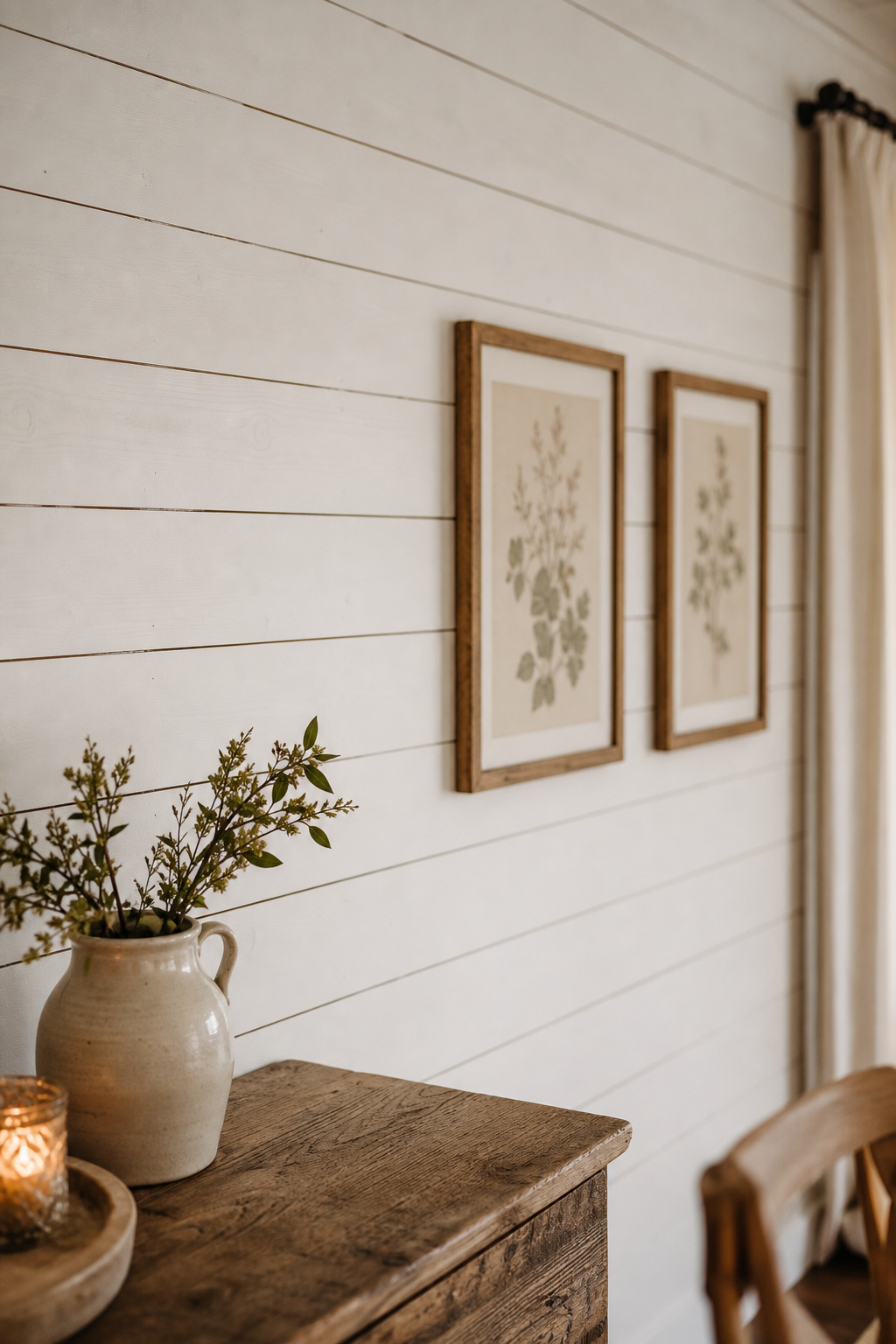 Horizontal warm-white shiplap accent wall in a rustic farmhouse dining room with botanical prints in natural wood frames and a reclaimed-wood sideboard below