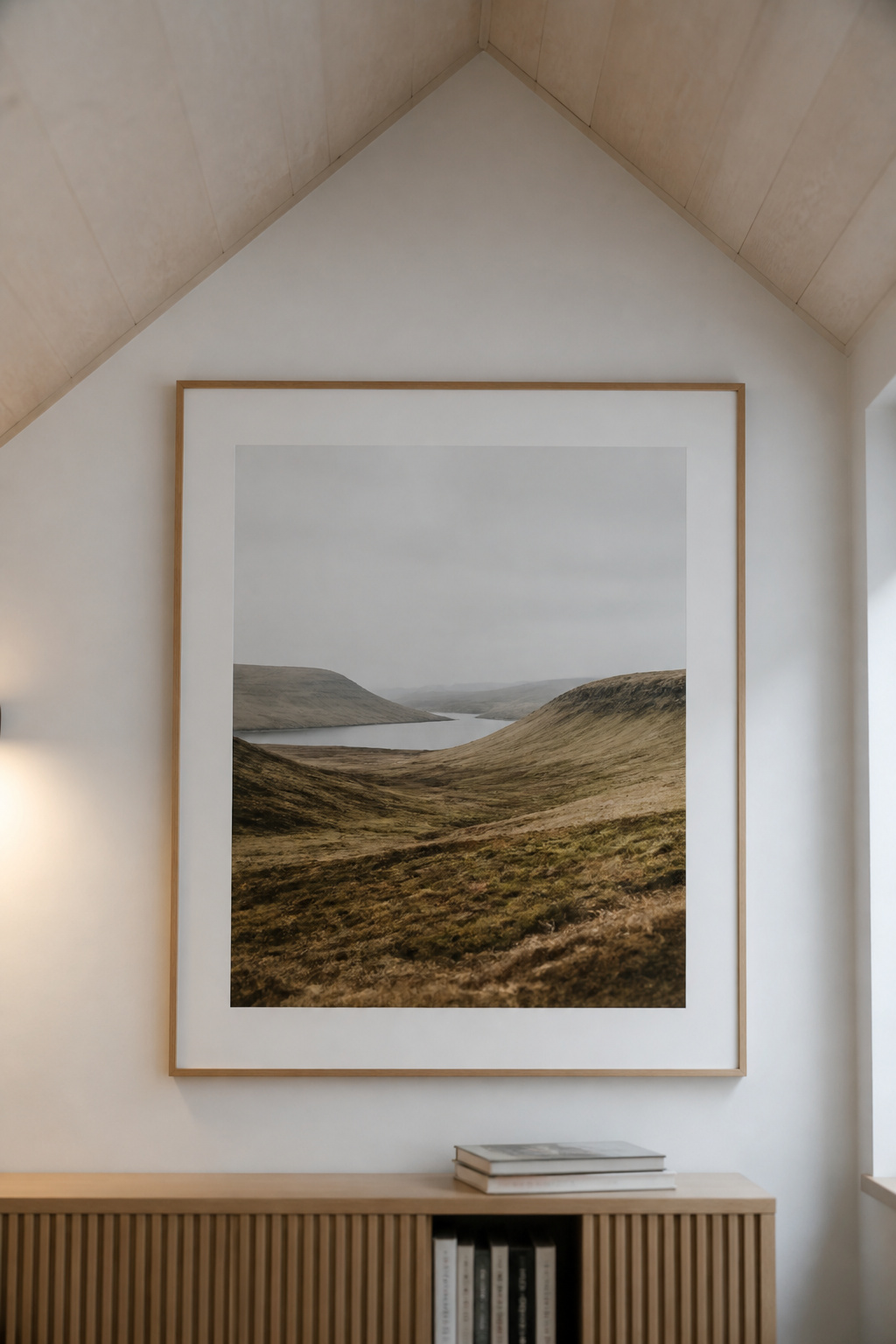 Single large framed landscape print hung just below the break point where a vertical white attic wall meets the sloped ceiling section