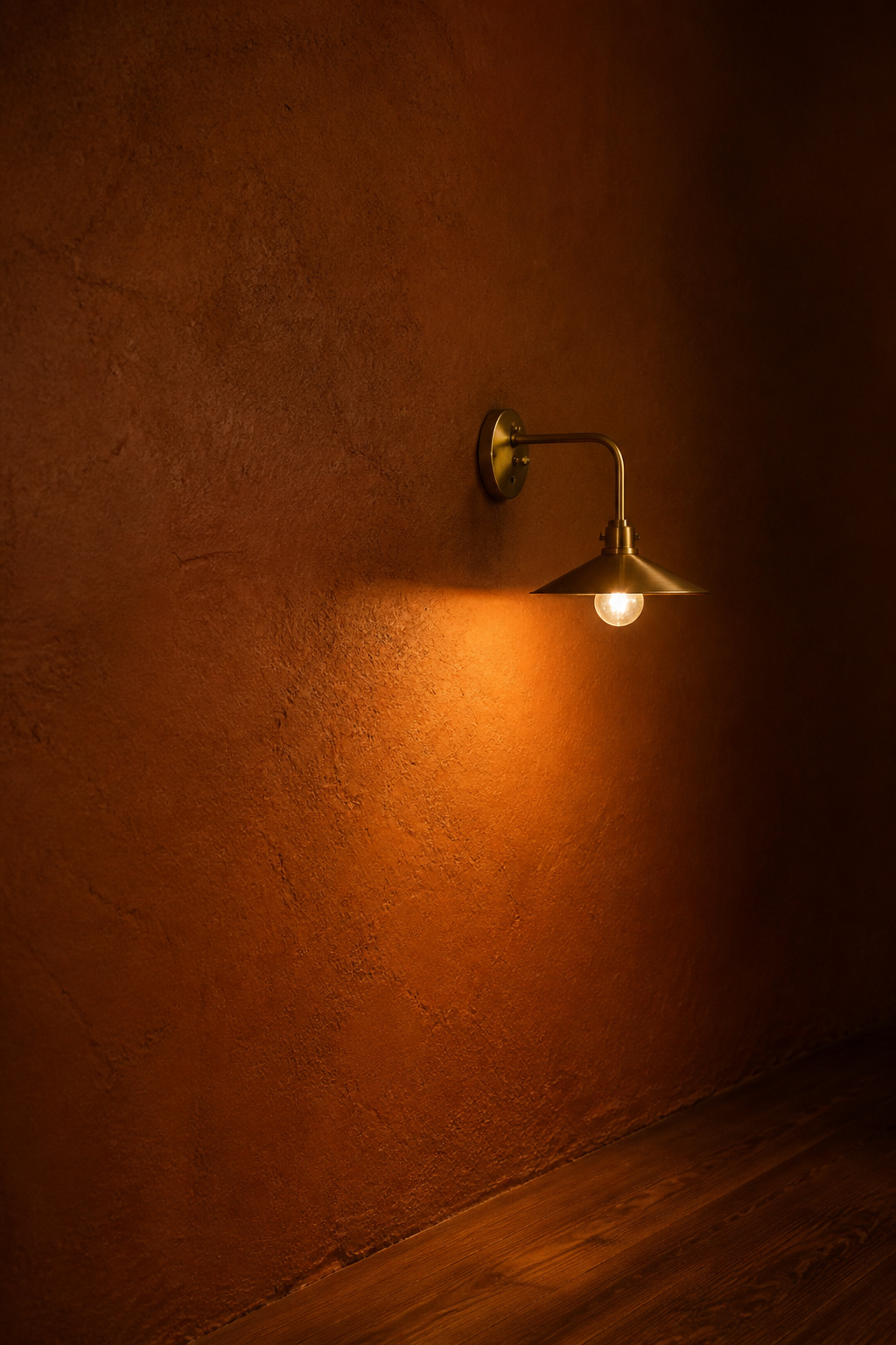 Close-up of a deep terracotta-brown matte painted wall with brass wall sconce and walnut floor sliver — warm moody paint palette study