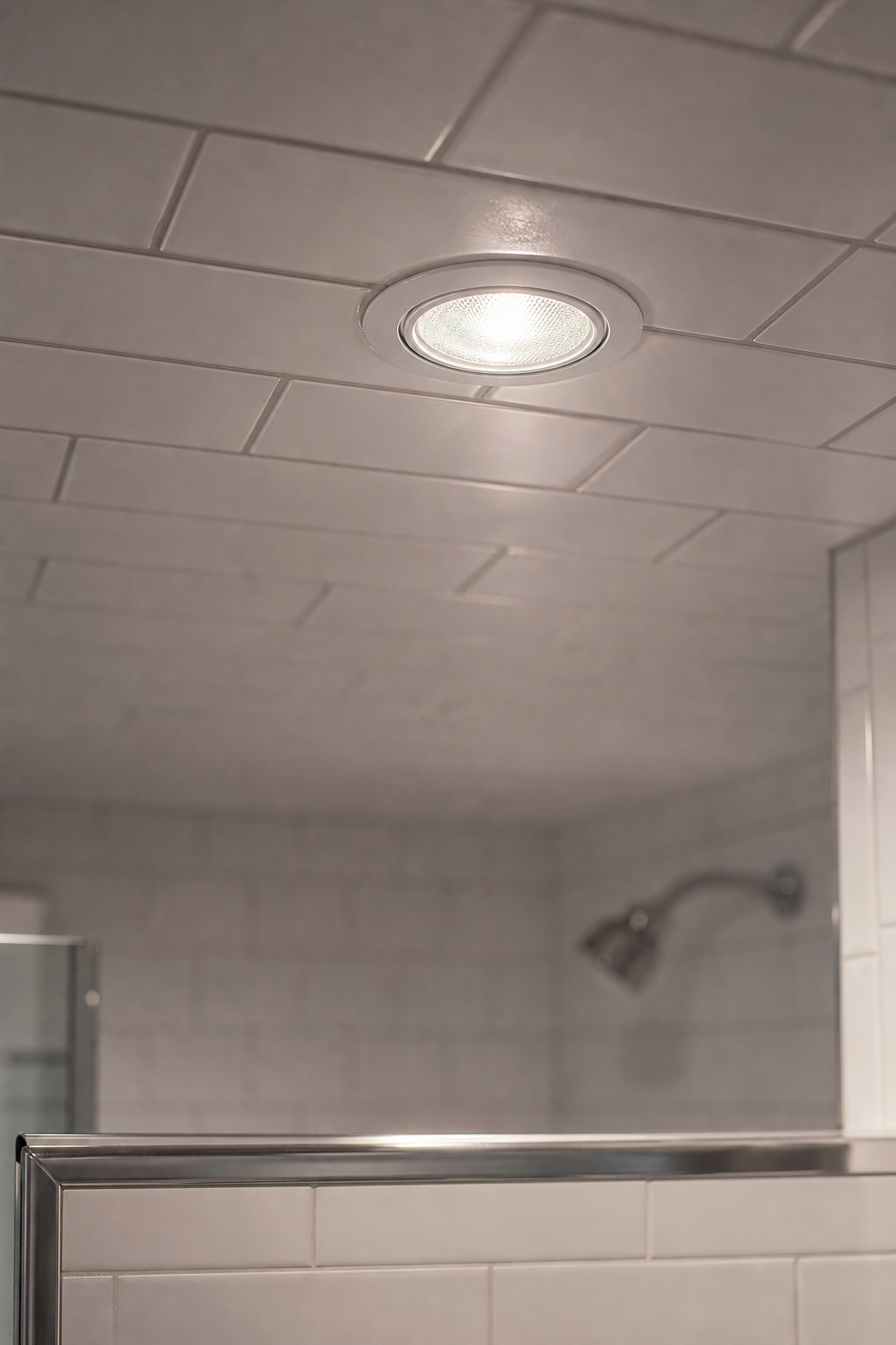 Wet-rated sealed gasketed recessed downlight mounted flush in white tiled shower ceiling inside shower enclosure
