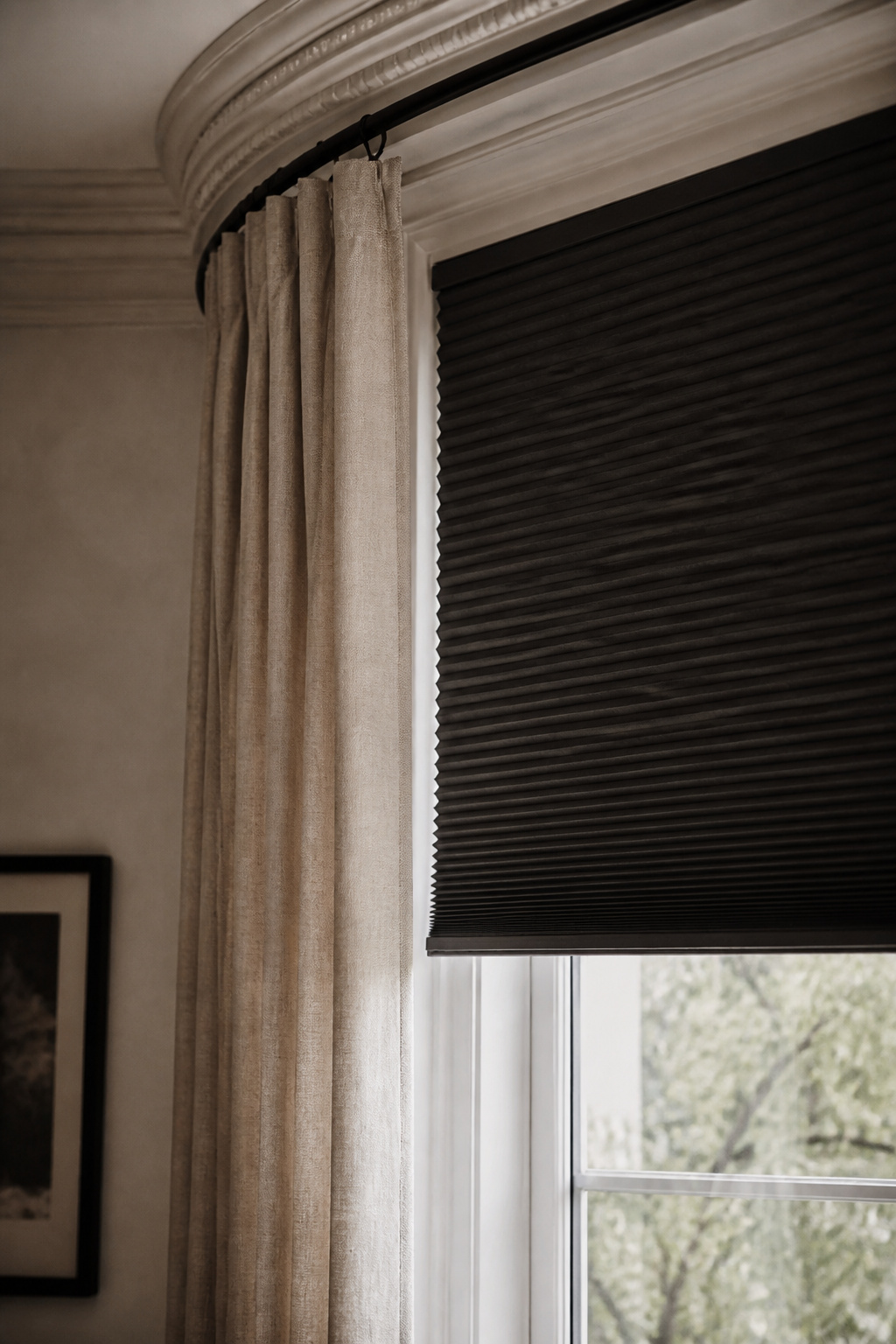 Blackout cellular shade layered under a linen curtain on a single bay window pane