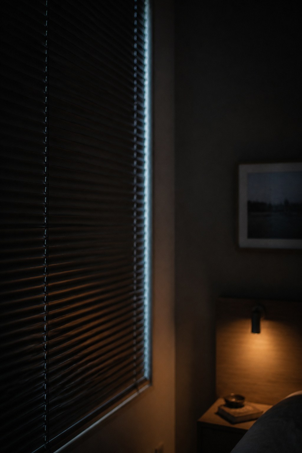 Closed bedroom venetian blind with a thin streak of outside light leaking along the edge at night