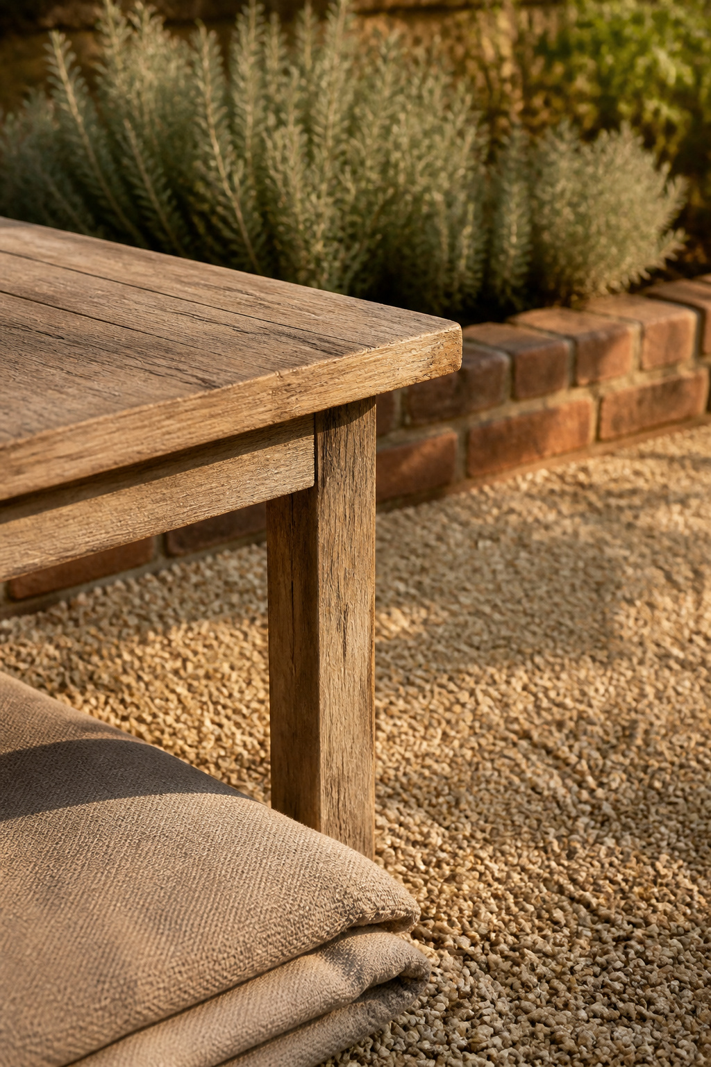 A modest buff gravel patio corner with a weathered oak side table and low brick edging