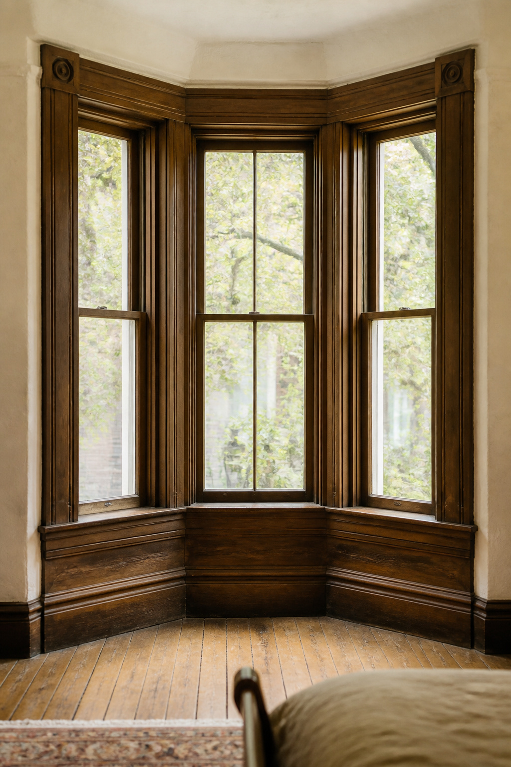 Canted three-sided bay window alcove with original period wood trim and mullions in a bedroom
