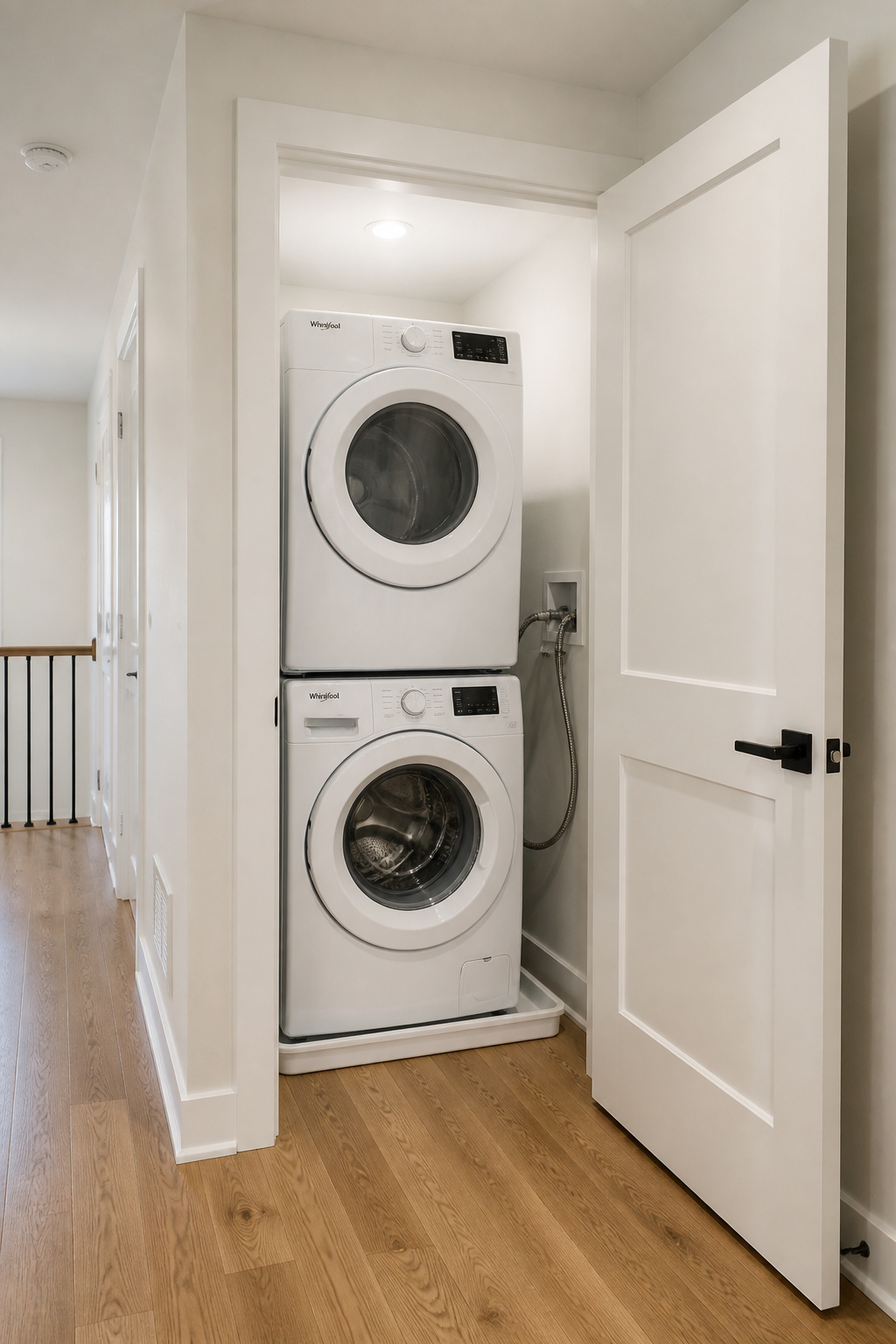 Completed closet-to-laundry room conversion with stacked washer dryer, drain pan, and braided hoses installed