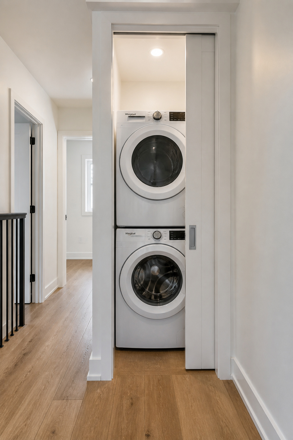Converted linen closet with stacked washer and dryer behind an open pocket door in an upstairs hallway
