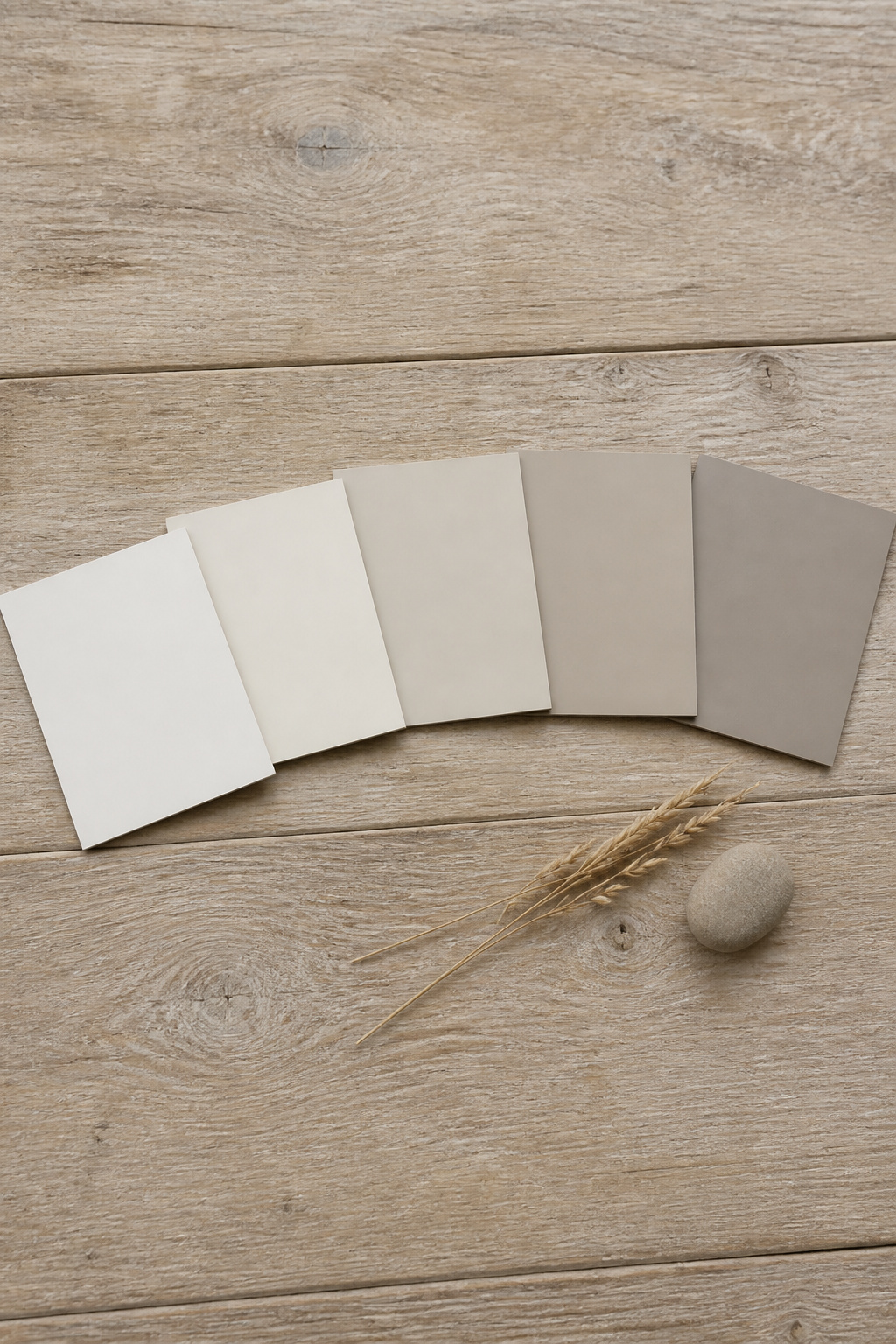 Five heritage neutral paint sample boards arranged on aged oak — progressing from warm white through creamy off-white to three mineral greiges, all suitable for a cottage entryway