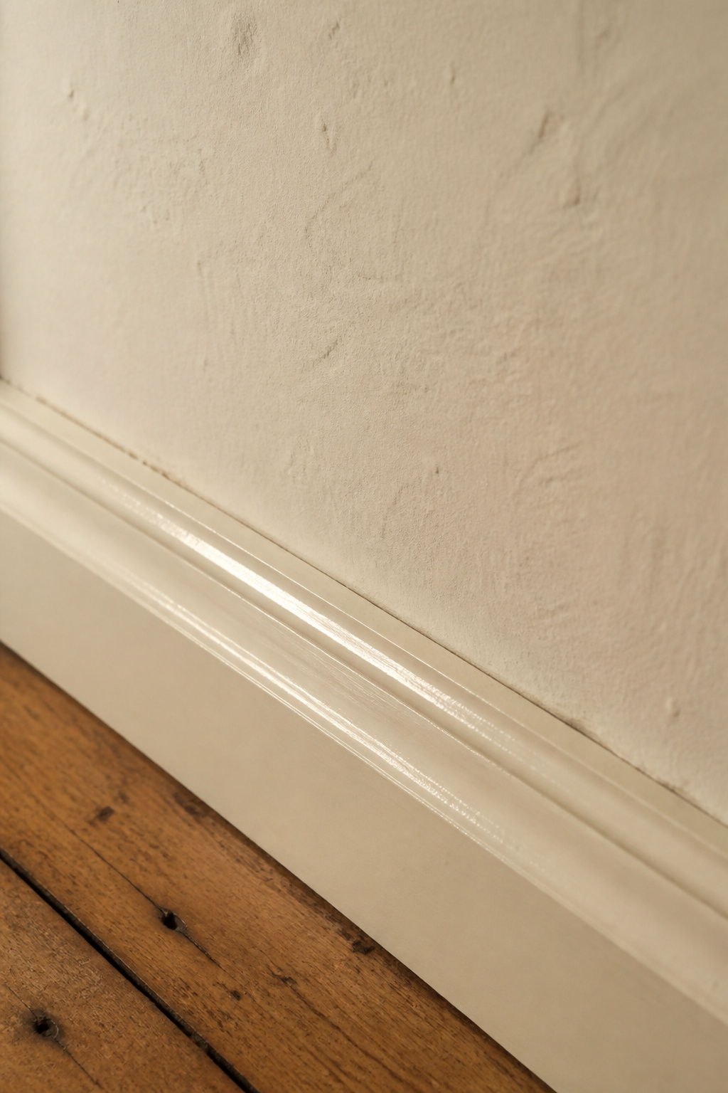 Close-up showing the sheen contrast between an eggshell warm-cream painted wall and a semi-gloss skirting board in the same colour in a period cottage entry