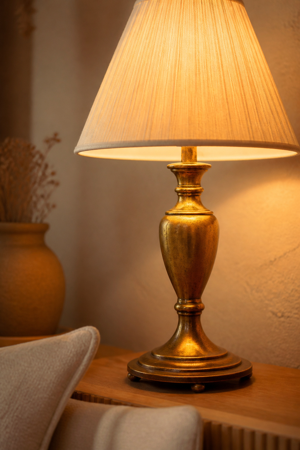 Aged brass bedside lamp glowing with warm 2700K light against an oatmeal wall next to a linen pillow