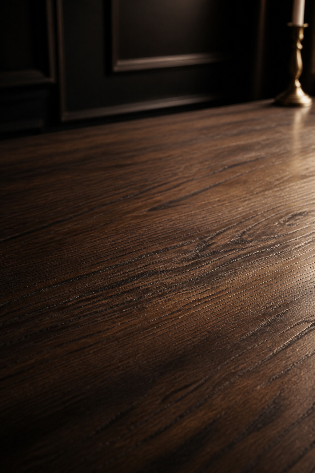 Close-up of dark walnut dining table grain showing figured open-grain pattern under warm sidelight