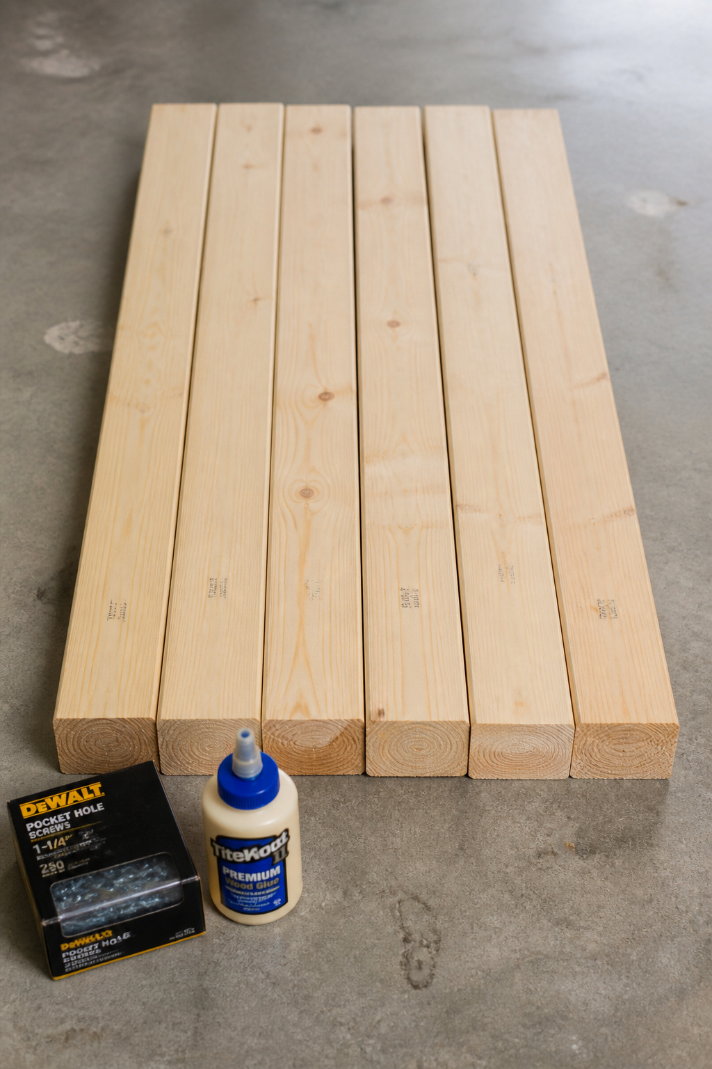 Flat-lay of six pine 2x4 boards with pocket-hole screws and wood glue arranged on a workshop floor before an entryway bench build