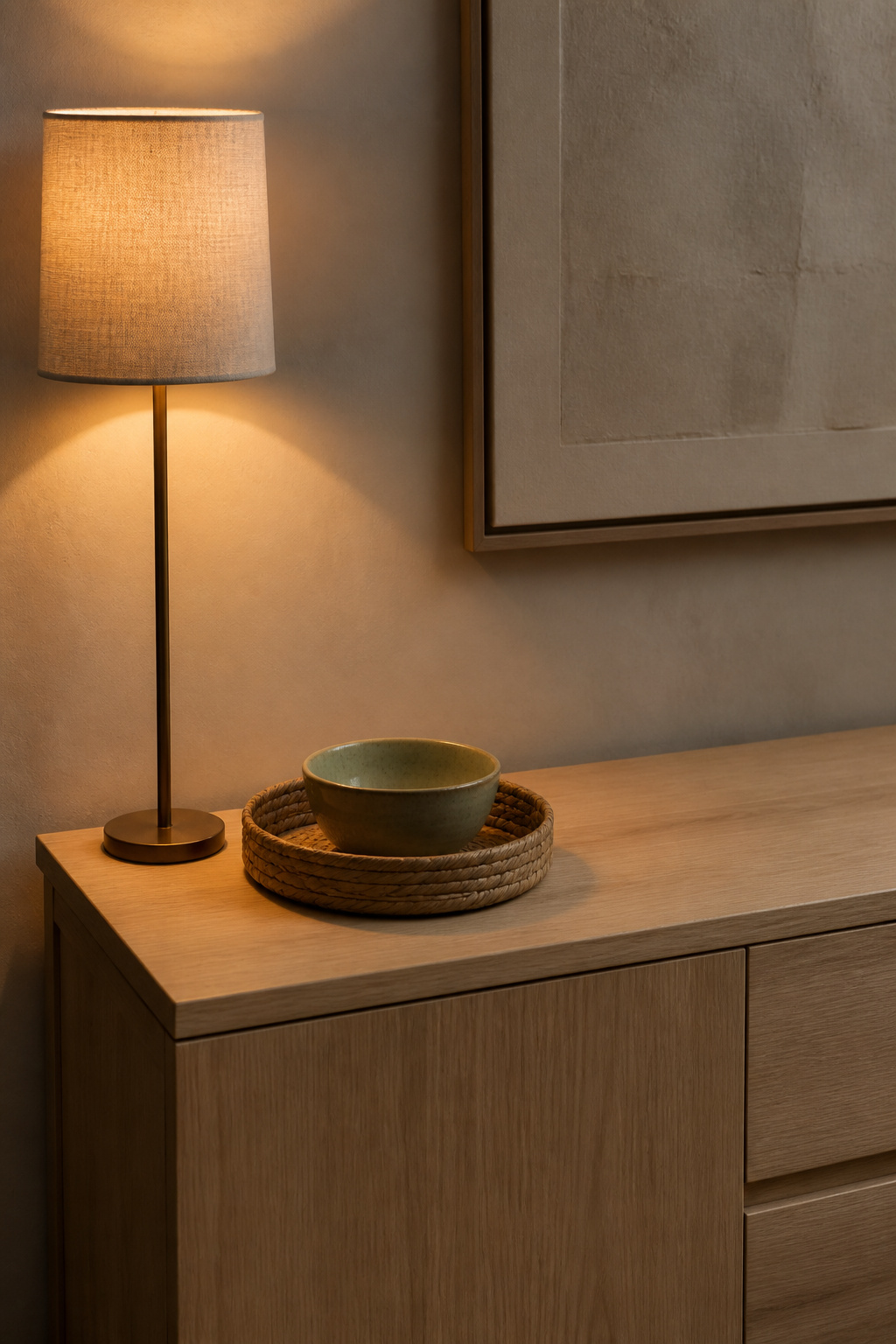Narrow sideboard end showing slim buffet lamp next to a round seagrass tray with ceramic bowl, rest of surface clear
