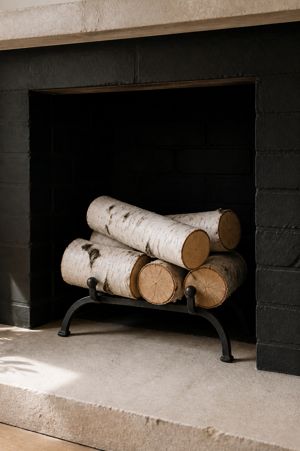 White birch logs stacked in two interlaced rows inside a dark-painted brick firebox on a wrought iron log cradle