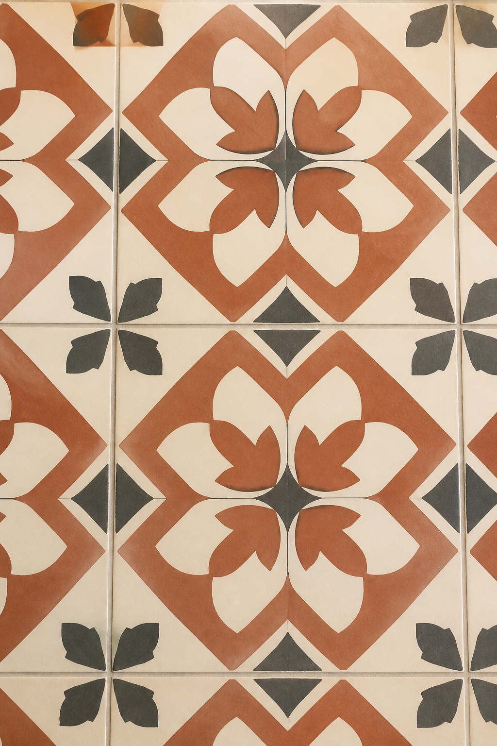 Close-up of encaustic cement floor tiles in terracotta, cream, and charcoal geometric pattern with matte surface and tight pale grout joints