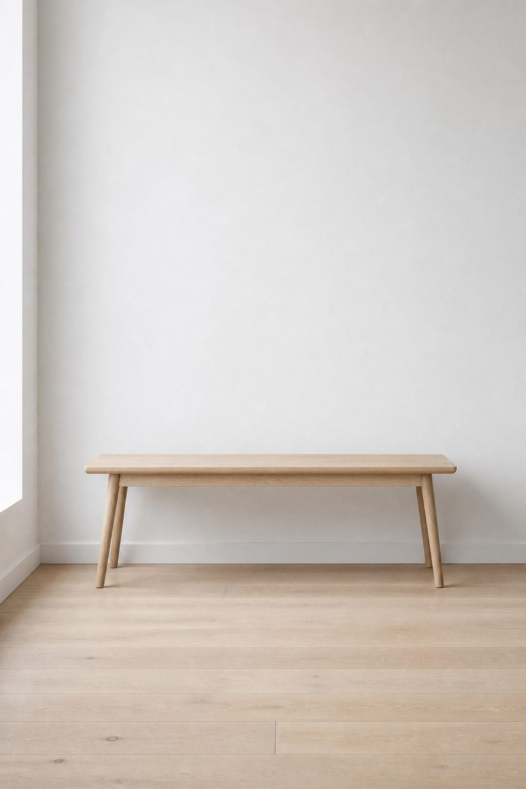 Pale oak entryway bench standing empty against a white wall, with clear floor space and bare wall above — the subtractive starting point for styling