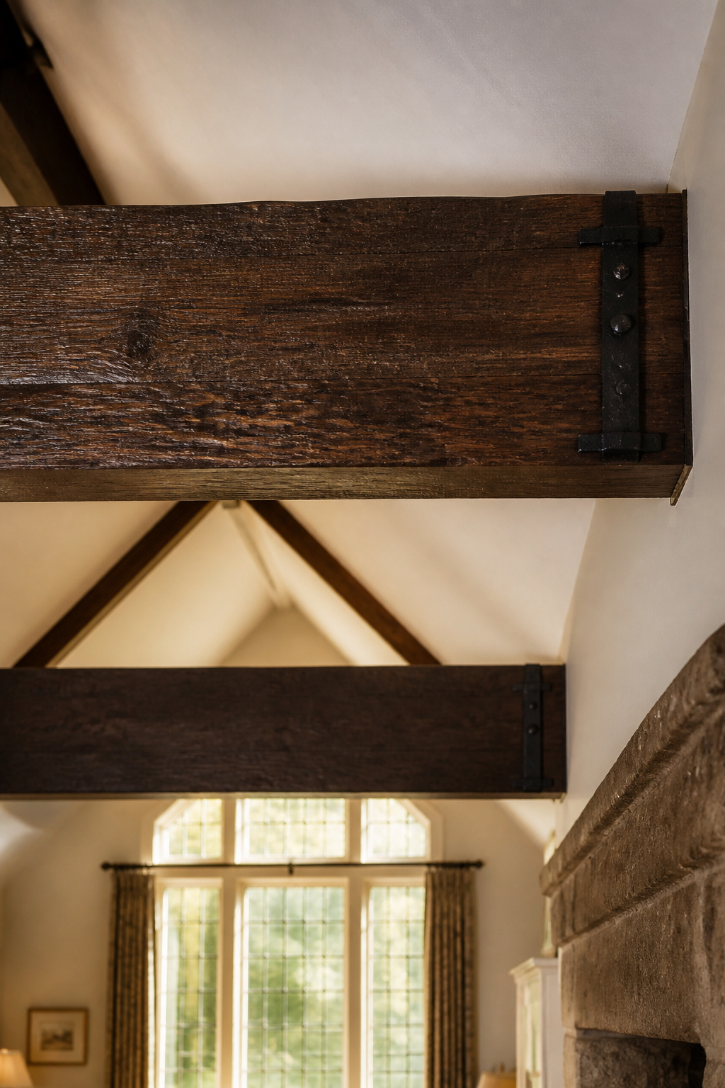 Vaulted living room with two full-width dark oak beams and iron strap brackets at the wall junction, Arts and Crafts style