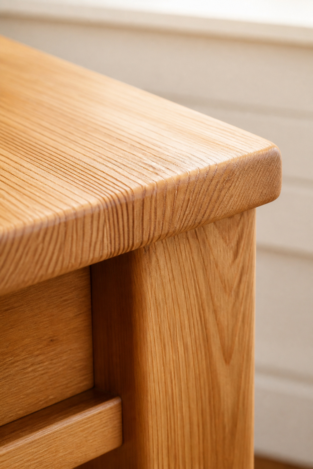 Close-up of a farmhouse bench corner showing grain pattern flowing continuously from the seat surface across the edge and down the leg — the hallmark of solid wood construction