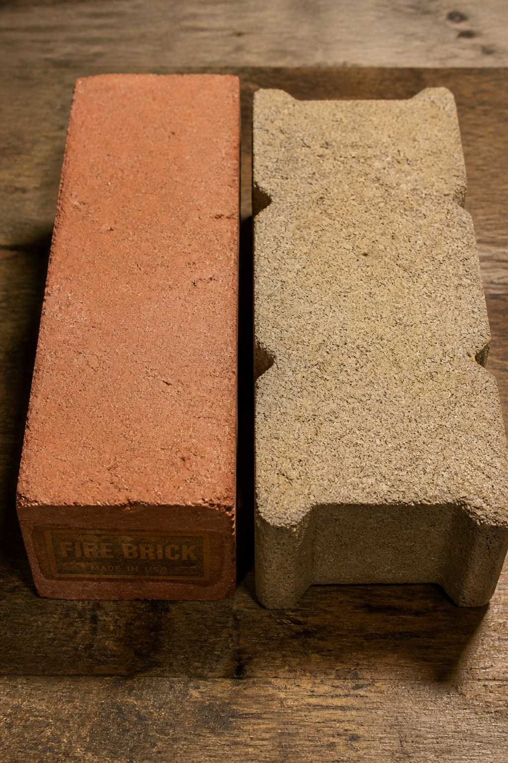 Side-by-side comparison of a dense red fire brick and a standard tan concrete retaining wall block on a workbench
