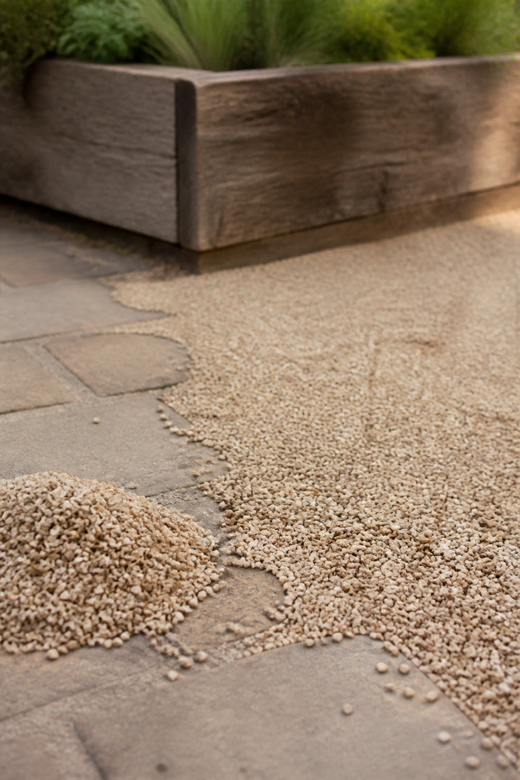 Buff pea gravel patio edge showing thin, migrated coverage next to a small pile of replacement stone