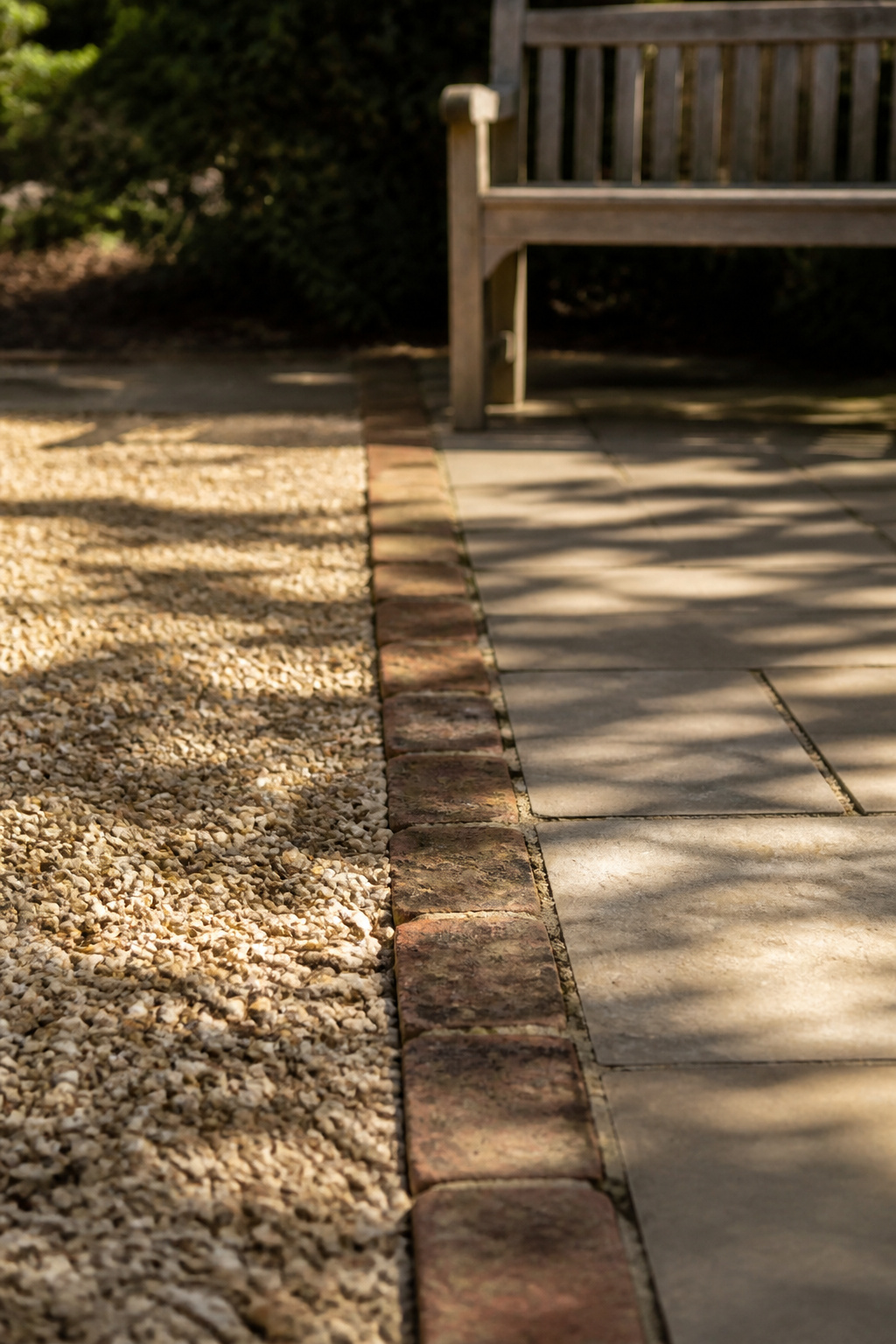 Oatmeal pea gravel patio meeting a paver walkway at an aged-brick edge, showing the texture difference