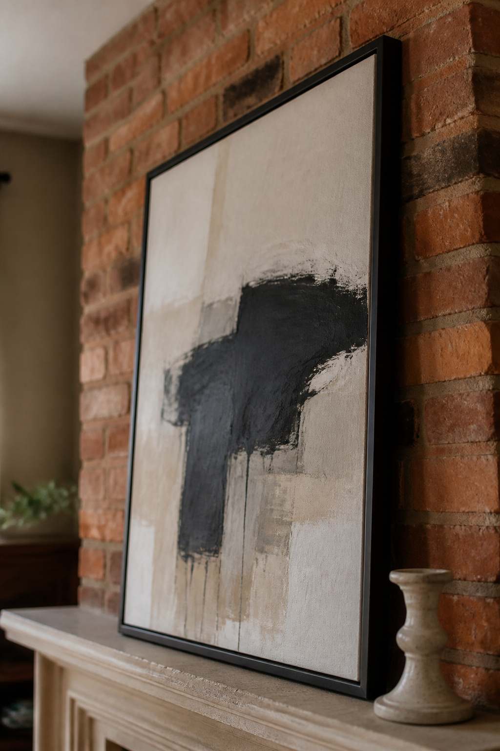 Large abstract canvas in simple matte-black frame leaning on brick chimney breast above a fireplace mantel