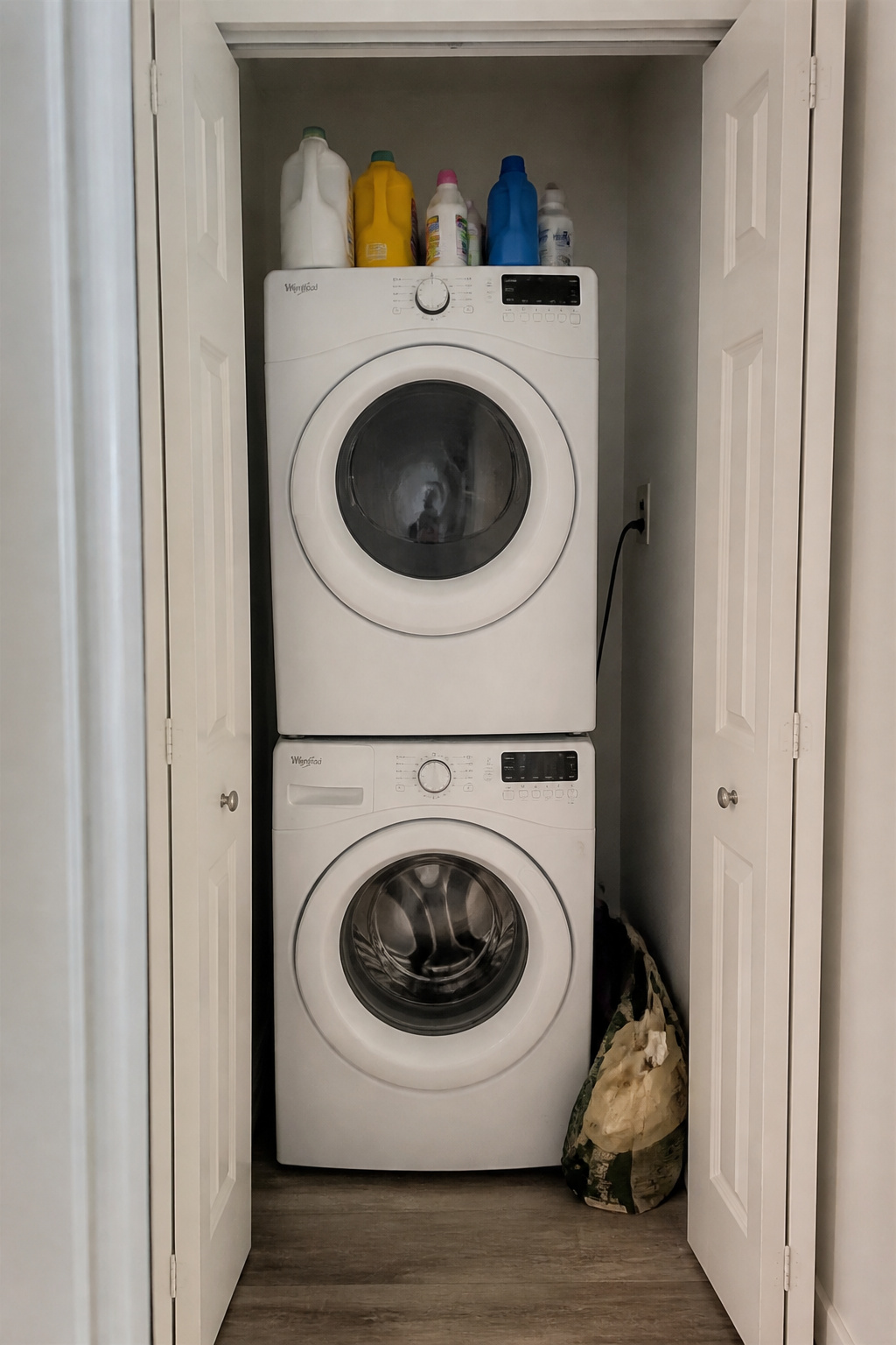 Narrow laundry closet alcove before organisation with items piled on top of stacked washer and dryer