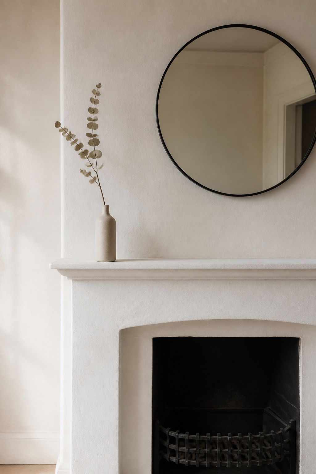 A minimalist mantel with a single eucalyptus branch in a slim vase placed to the left third, with the rest of the shelf bare, showing how off-centre placement creates intentional asymmetry