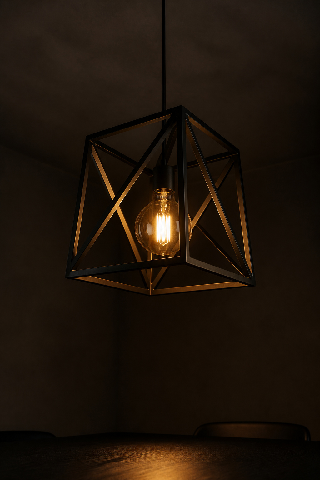Geometric matte-black cage pendant lit with warm amber glow over a dark dining table against warm-graphite ceiling