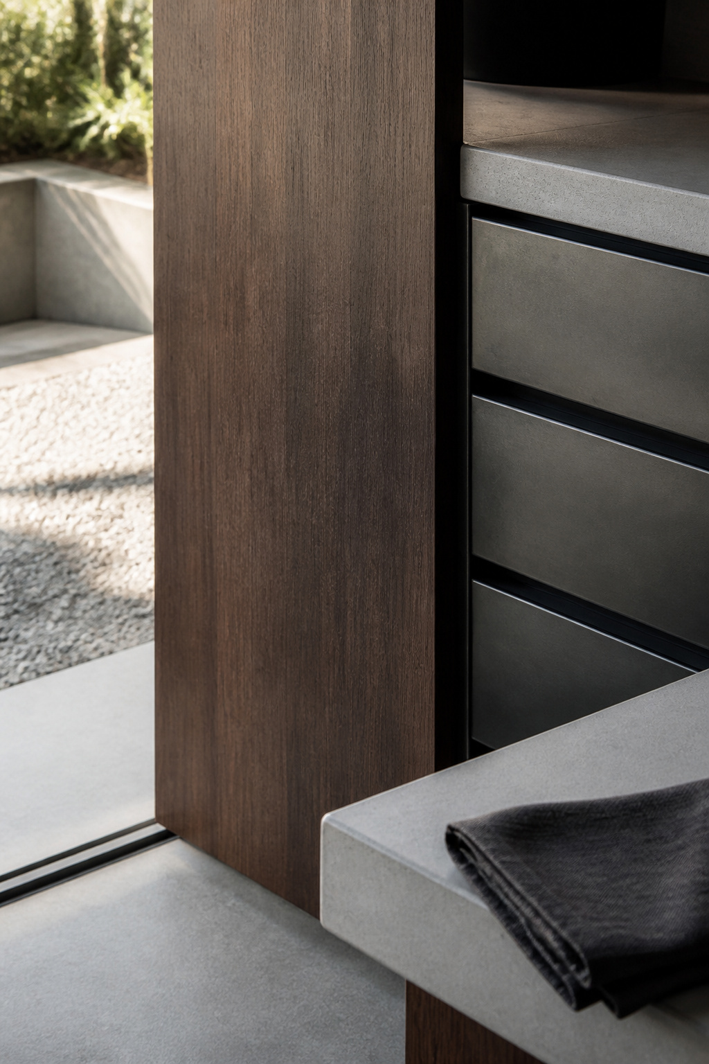 Dense ipe wood accent panel beside blackened steel cabinetry and pale concrete counter in a modern outdoor kitchen