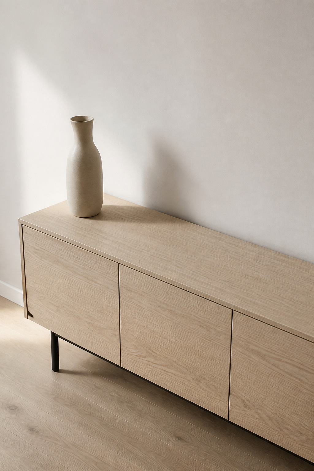 A pale sideboard with almost nothing on its surface except one matte cream ceramic vessel, showing how removal before placement is the first principle of modern sideboard styling