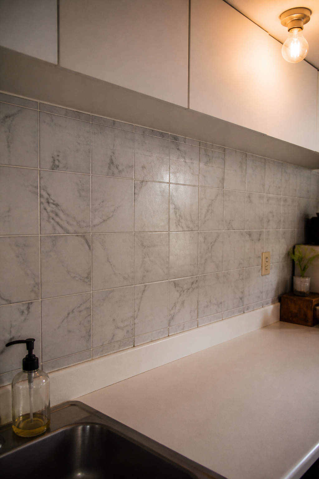 Neutral grey marble-patterned peel-and-stick backsplash tiles on a rental kitchen wall running from countertop to cabinet bottom
