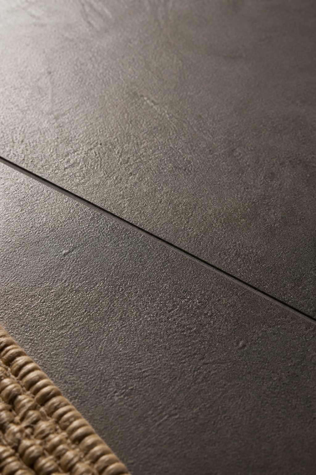 Close-up detail of matte textured charcoal porcelain tile showing fine surface grain and tight grout line in a residential entryway