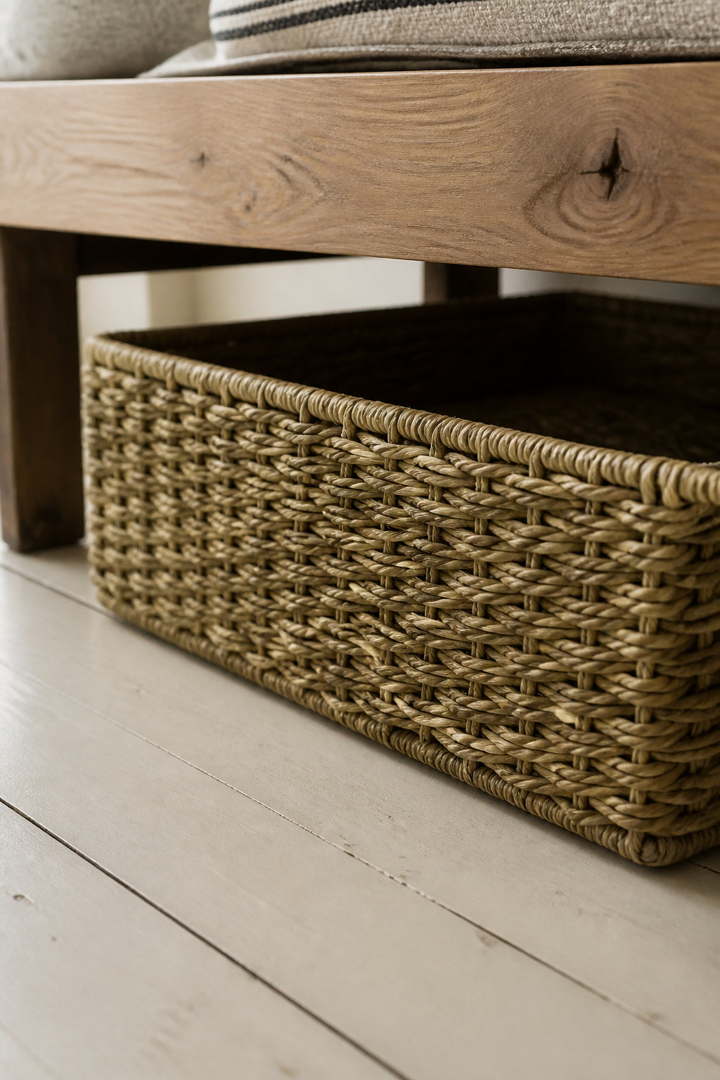 A large rectangular seagrass basket positioned under the shelf of a farmhouse entryway bench, showing the flat weave texture against the pine bench apron