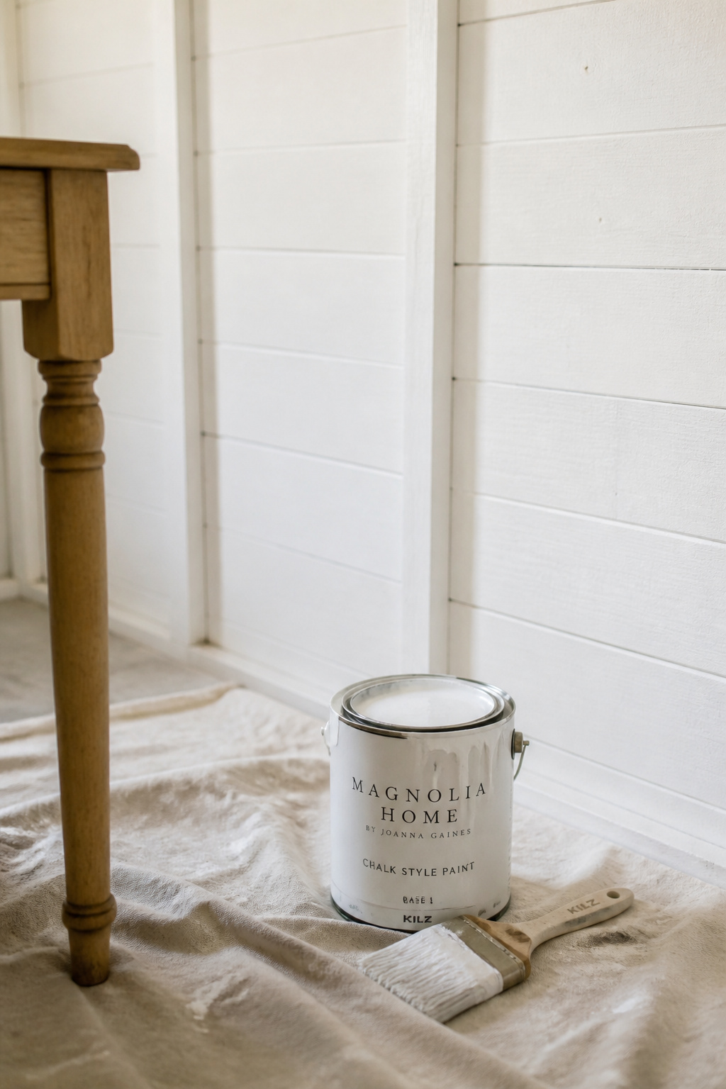 A freshly painted white she shed wall with paint roller and brush resting on a drop cloth