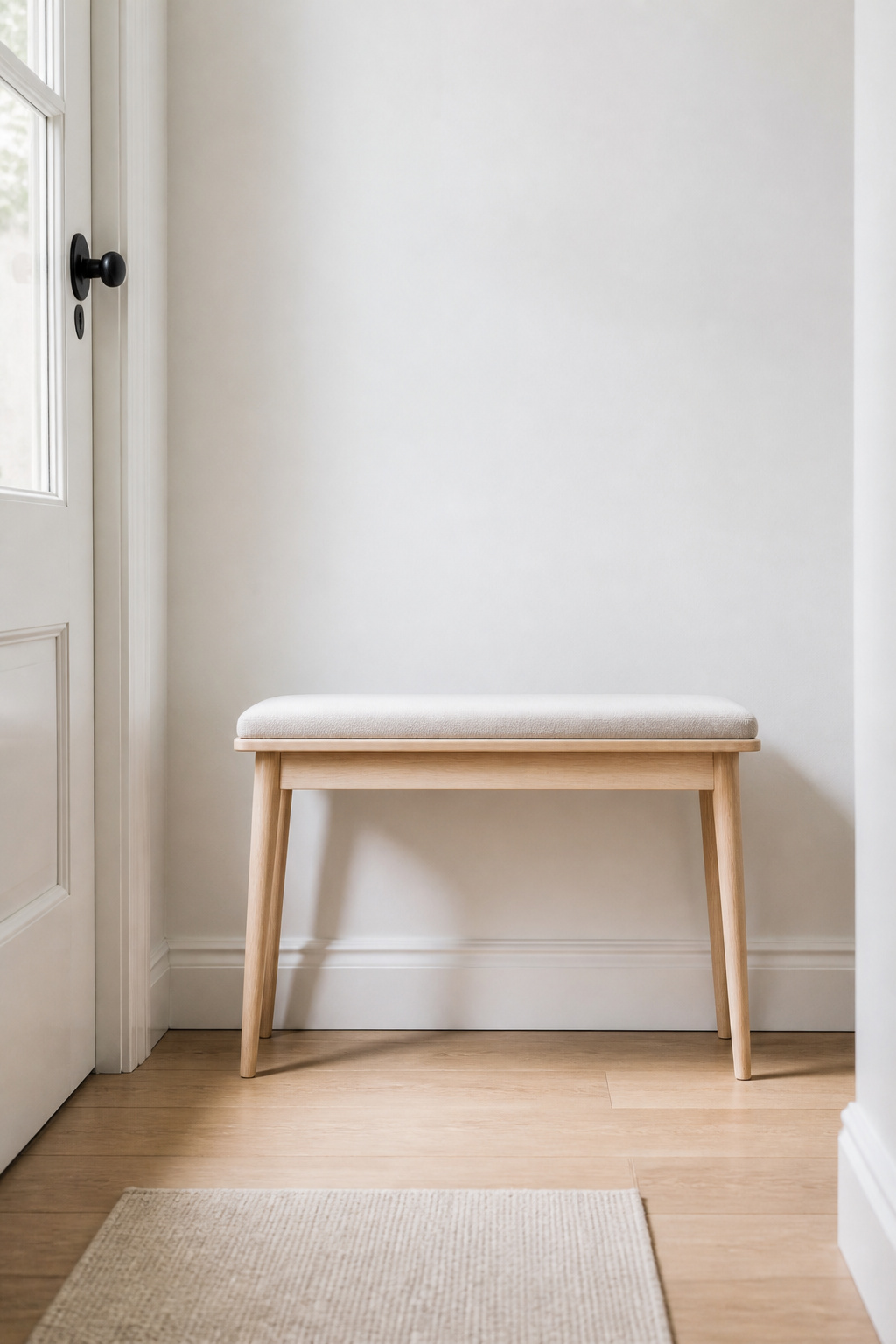 36-inch pale birch entryway bench with tapered legs positioned centrally on a white hall wall, one linen cushion on the seat, clear floor in front