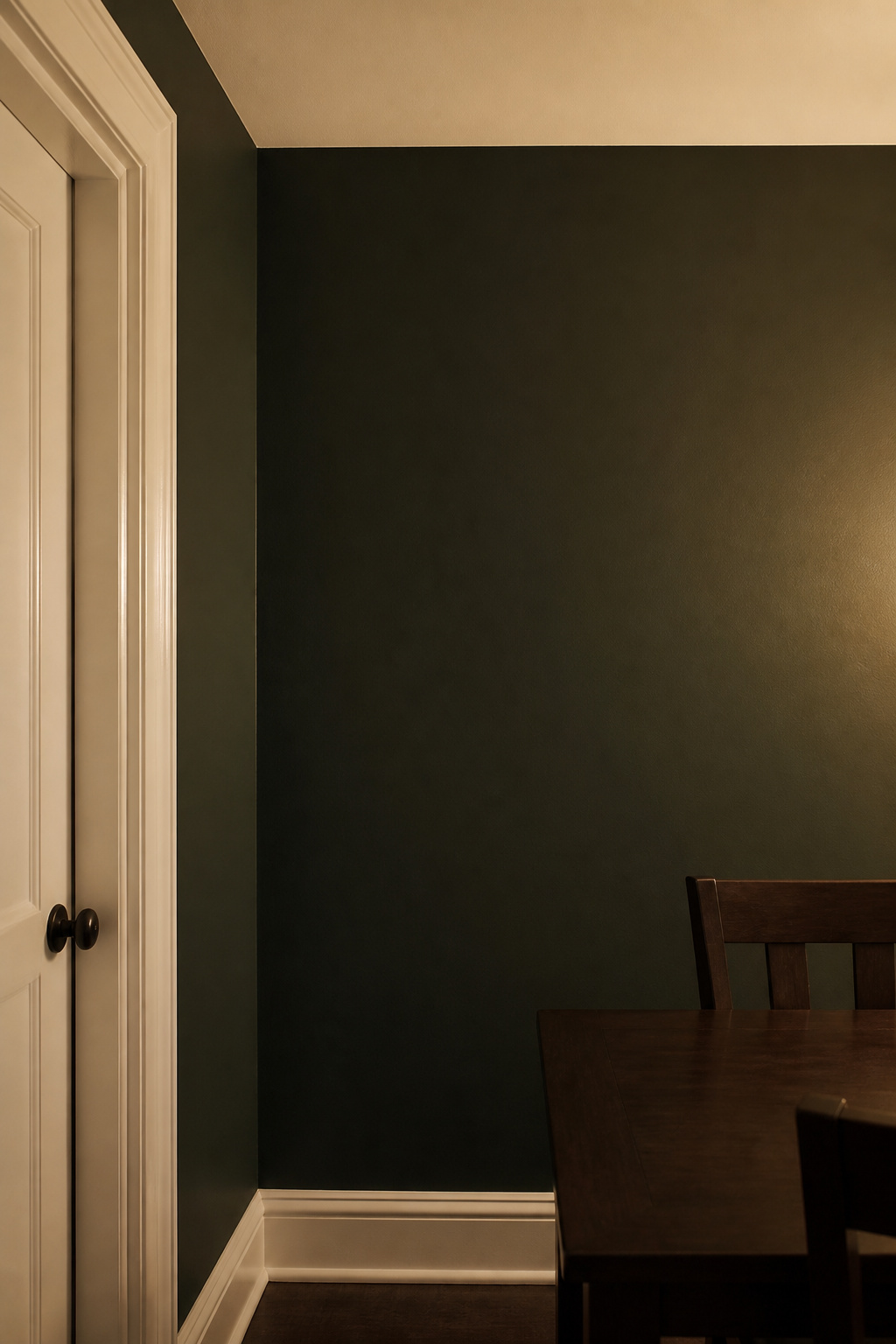 Dark green dining room wall corner with crisp warm white ceiling and semi-gloss white door trim, showing the contrast technique for small dark rooms