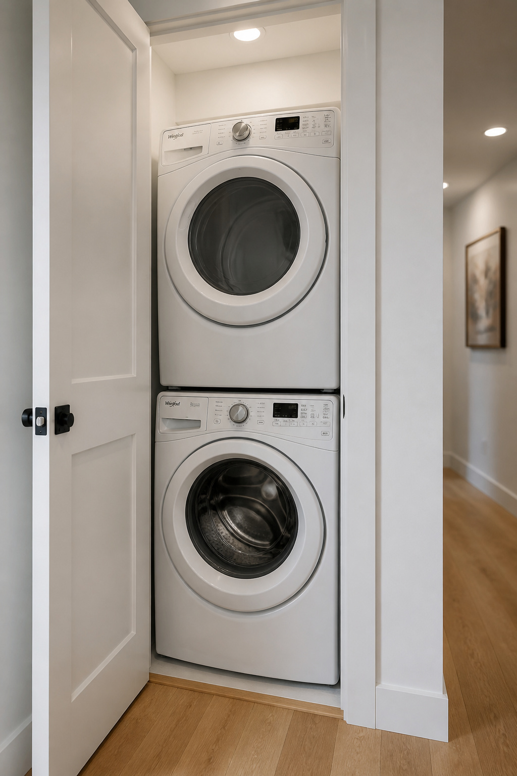Stacked white front-load washer and dryer inside a narrow white-painted closet, converted from a linen cupboard