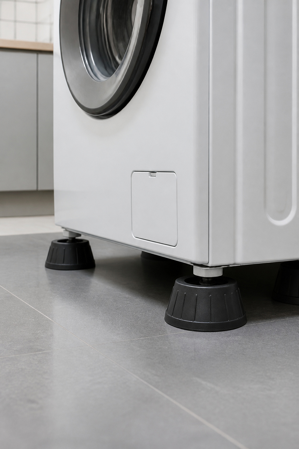 Black rubber anti-vibration pads beneath the four feet of a white front-load washing machine on a tile floor