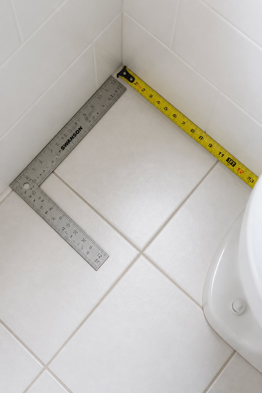 Top-down view of a bathroom corner with a carpenter's square checking the wall angle before fitting a corner shelf