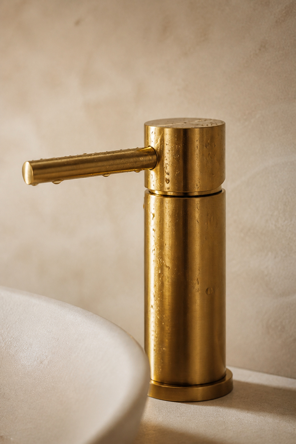 Water droplets beaded on a brushed brass bathroom faucet handle against a microcement wall