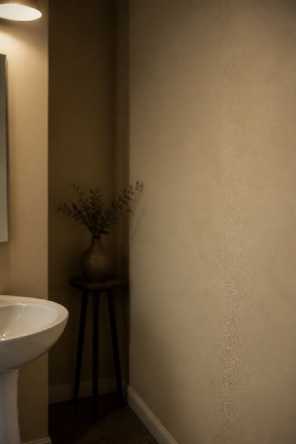 Small windowless powder room painted pale beige looking dim and flat under a single overhead light