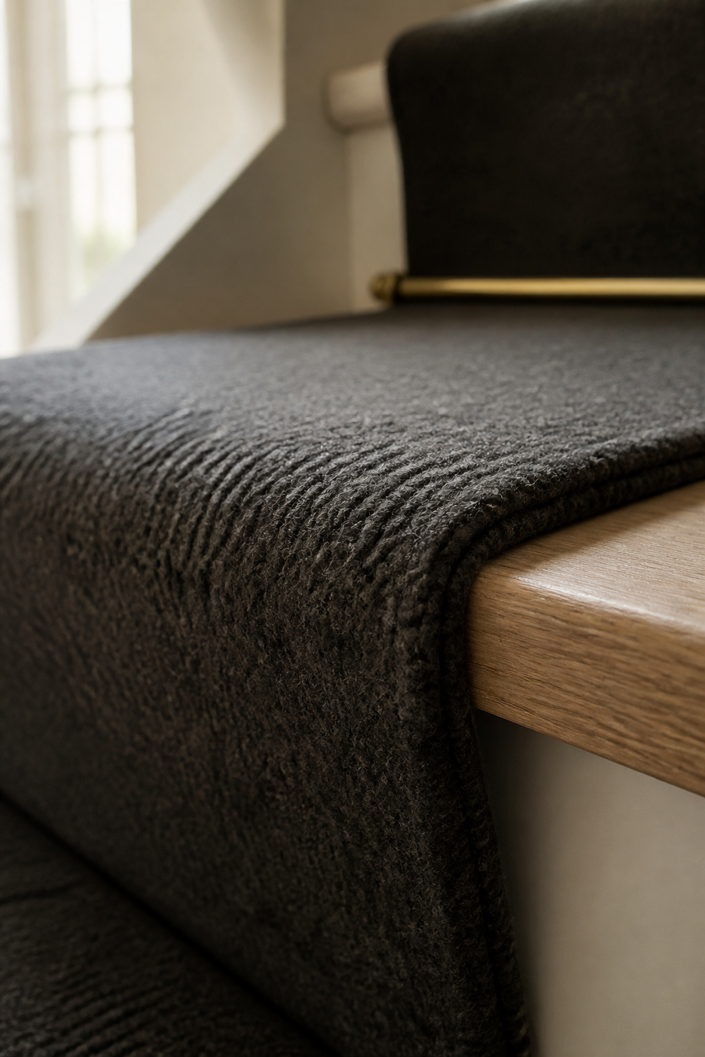 Close-up detail of a dense wool stair runner wrapped over a tread nosing with natural oak visible at the edge